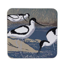 A square coaster with rounded corners featuring a Sue Welfare print of three black-and-white avocets in a marshy water setting with blue water and beige reeds.