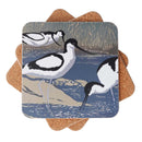 A square cork coaster with rounded corners, featuring a printed illustration of three black-and-white wading birds in a marshy water scene. The coasters are stacked in a fan-like arrangement on a plain white background.