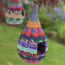Colorful woven birdhouse hanging outdoors with a blurred natural background