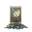 A playing card sized jigsaw puzzle box standing upright with several loose puzzle pieces scattered in front on a plain white background. The puzzle box shows a Blue tit on a branch.