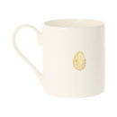 An off-white ceramic mug featuring a small, realistic printed Easter egg design on the front, set against a plain white background.