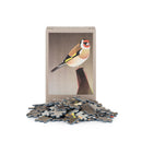 A 99-piece jigsaw puzzle box standing upright on a white background, with several loose puzzle pieces scattered in front. The box features a Goldfinch bird perched on a branch.