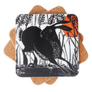 A square printed coaster with rounded corners sits on top of three circular cork coasters against a plain white background. The top coaster features a black-and-white linocut-style illustration of a hare among reeds, with a bright orange sun in the upper right.