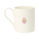An off-white ceramic mug featuring a small, realistic brown speckled egg illustration on the side, set against a plain white background.
