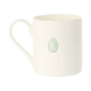 An off-white ceramic mug featuring a small, light green oval stone inlaid on the side, set against a plain white background.