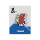 A wooden pin badge featuring a vole holding a green strand of grass, mounted on a branded display card.