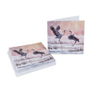 A stack of greeting cards and a single card displayed on a white background, both featuring a winter landscape illustration of two cranes in flight over a snowy field under a pink and peach sky.