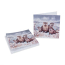 A stack of greeting cards and a single card displayed on a white background, both printed with an illustration of several otters sitting in a snowy outdoor scene.